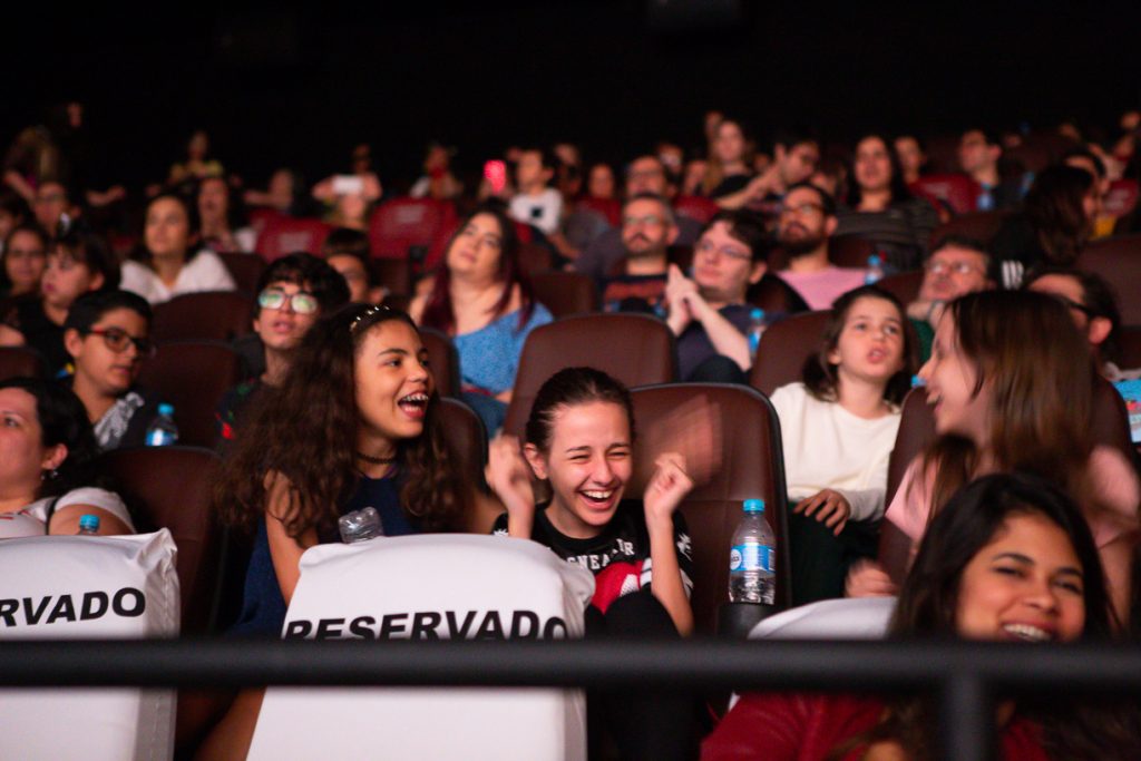 Imagem da plateia do cinema mostra, em primeiro plano, crianças rindo durante a exibição.
