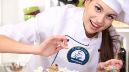Imagem de uma confeiteira com chapéu de cozinheiro, colocando confeitos em um bolo.