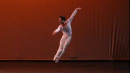imagem de bailarino no palco, em um salto com as pernas agrupadas.