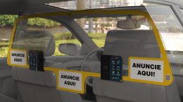 Imagem mostra a placa de acrilico instalada, vista a partir do banco traseiro do carro. Ela tem três espaços com indicaçao "anuncie aqui".