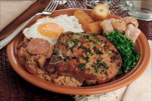 Imagem de um prato de cerâmica com o tradicional virado à paulista: couve, carne, torresmo, arroz, tutu de feijão e ovo frito.