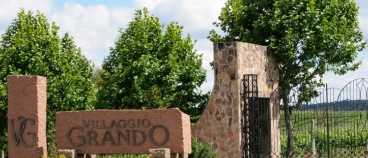 muro de pedra da vinícola, com portões de ferro abertos e o nome inscrito em placa também de pedra.