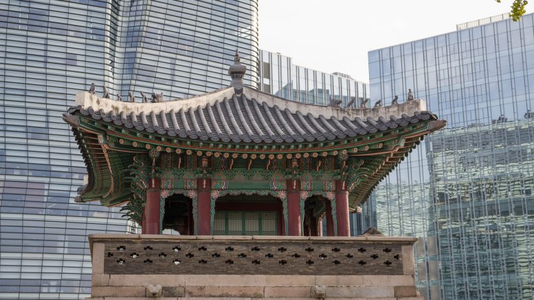 imagem da parte de cima de um templo coreano em primeiro plano e atrás predios modernos com fachada de vidro.
