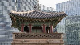 imagem da parte de cima de um templo coreano em primeiro plano e atrás predios modernos com fachada de vidro.