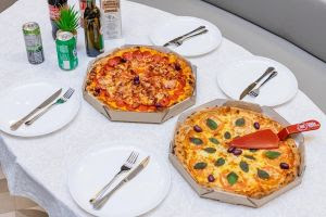 imagem de uma mesa posta, com duas pizzas, pratos, talheres e refrigerantes