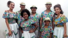 imagem de um conjunto de cinco jovens e três crianças, com roupas em tecido florido. todos posam para a câmera.