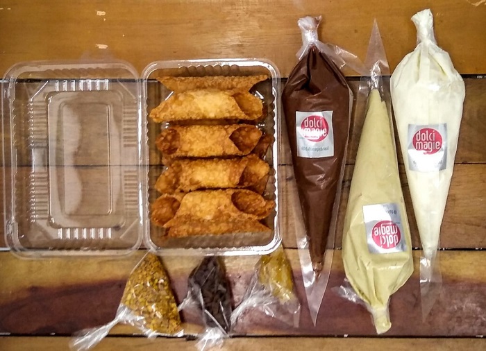imagem do kit cannoli, uma das sugestões de sabores italianos para as festas: em uma embalagem os rolinhos de massa, três bisnagas com recheios e três saquinhos de castanhas