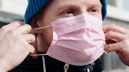 imagem de um jovem colocando uma máscara segurando corretamente pelos elásticos.