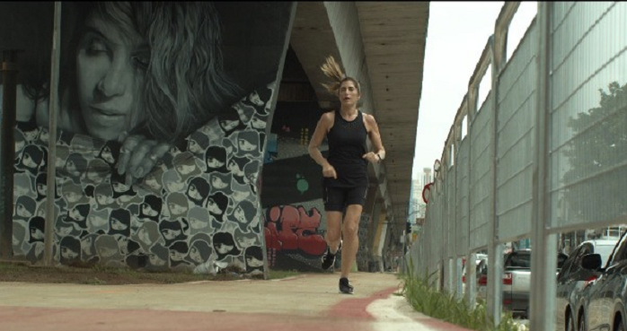 imagem do filme de promoção da corrida e caminhada solidária, mostra mulher vista de trás, correndo em canteiro central de avenida