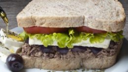 sanduíche vegetariano visto de lado, em pão de forma integral, com queijo branco, azeitonas pretas, alface e tomate.