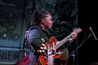 imagem com visão 'obliqua' de Marlene, tocando guitarra, em um palco com louca luz