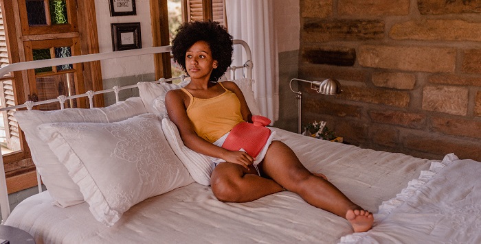 mulher sentada em uma cama aplicando uma bolsa de água quente na perna