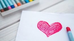 imagem de uma folha branca com coração desenhado com crayon e uma caixa de lápis crayon ao lado.