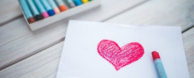 imagem de uma folha branca com coração desenhado com crayon e uma caixa de lápis crayon ao lado.
