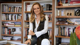 isabelle anchieta, curadora do café filosófico, posa sentada em frente a uma parede-estante de livros
