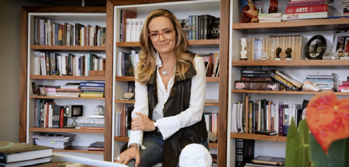 isabelle anchieta, curadora do café filosófico, posa sentada em frente a uma parede-estante de livros