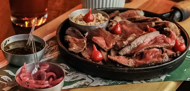 imagm de um prato com diversas carnes e algumas pimentas biquinho, sobre uma mesa de madeira.