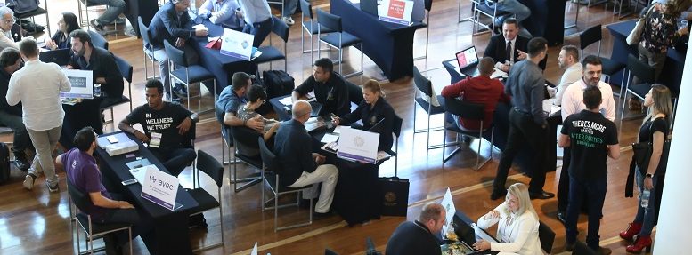 imagem aérea da feira de franquias com diverss mesas em um salão de hotel e pessoas em reunião em cada uma delas.