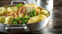 Imagem de uma caçarola de alumínio baixa, com o prato pronto: bacalhau, batatas e verduras.