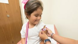 imagem de menina sentada sorrindo ao colocar um bandaid colorido após a vacinação infantil.
