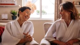 imagerm de duas mulheres de roupão, sentadas conversando e sorrindo no Dia dos Amigo