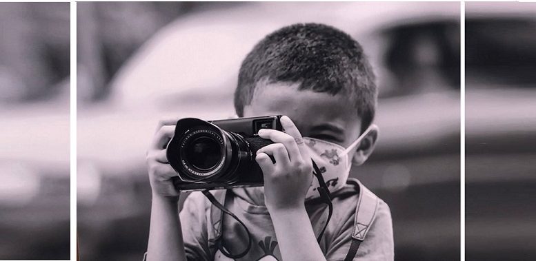 imagem em preto e branco de menino do MTST segurando uma camera fotográfica profissional, ele tem cabelo bem curto e usa márcara