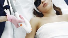 mulher deitada com óculos de proteção realizando depilação a laser