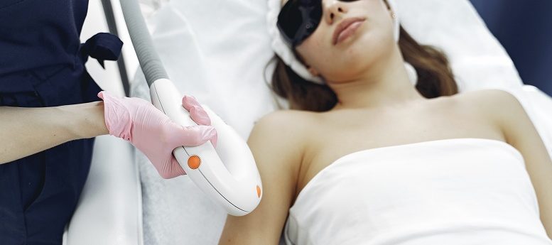 mulher deitada com óculos de proteção realizando depilação a laser