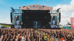 palco do lollapalooza de 2020 visto por trás do publico que está todo com braços erguidos. o céu está muito azul