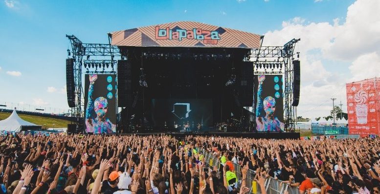 palco do lollapalooza de 2020 visto por trás do publico que está todo com braços erguidos. o céu está muito azul