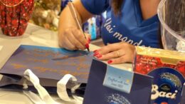 detalhes das mãos de uma calígrafa personalizando sacolas de papel azul, em primeiro plano uma sacola de ovo de pascoa da marca baci perugina