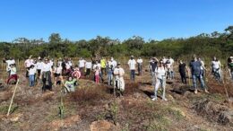 grupo de pessoas posa com picaretas em uma área descampada de um parque, é dia, o ceu está azul sem núvens e faz sol.