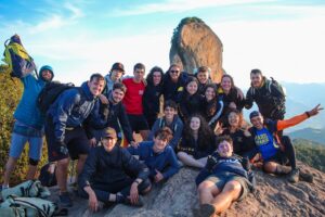 acampantes do Paiol Grande posam para foto em cima do Bauzinho, com a Pedra do Bau ao fundo