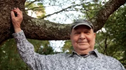 joao donato de boné, sorrindo em frente a uma árvore