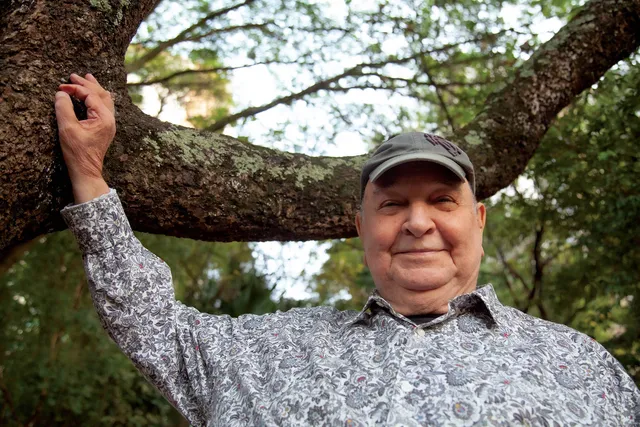 joao donato de boné, sorrindo em frente a uma árvore