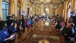 pessoas sentadas à mesa em reunião em uma salão preservado, com aspecto centenrário