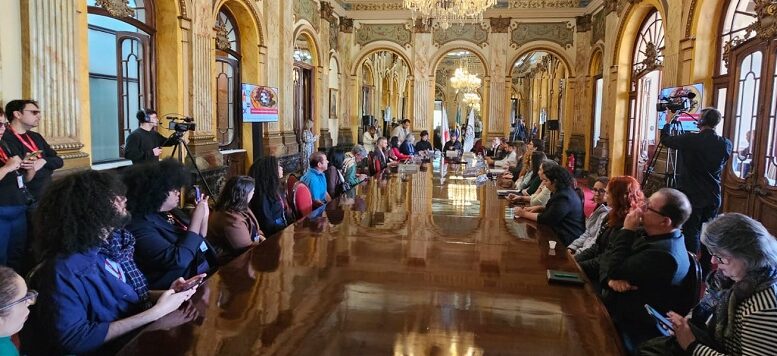 pessoas sentadas à mesa em reunião em uma salão preservado, com aspecto centenrário