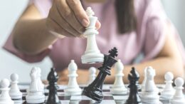 imagem aproximafa de um tabuleiro de xadrez em que se vê um jogdor com peça branca derrubando o rei preto.