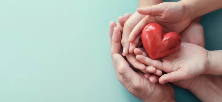 imagem de mãos de adulto em concha com mãos de criança dentro e um coração sendo segurado por elas