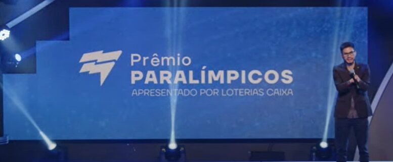 Yohansson Nascimento no palco em frente a uma tela em que se le premio paralimpicos apresentado por loterias caixa