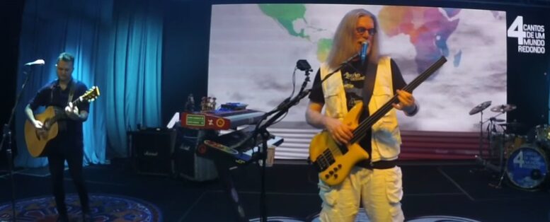 humberto gessinger no palco tocando, atrás um telão com uma imagem do mapa mundi, há outro musico no palco