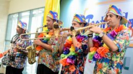 bandinha de carnaval: quatro musicos com instrumentos musicais, lado a lado, com camisas coloridas, chapéus e colares havaianos.