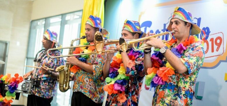 bandinha de carnaval: quatro musicos com instrumentos musicais, lado a lado, com camisas coloridas, chapéus e colares havaianos.