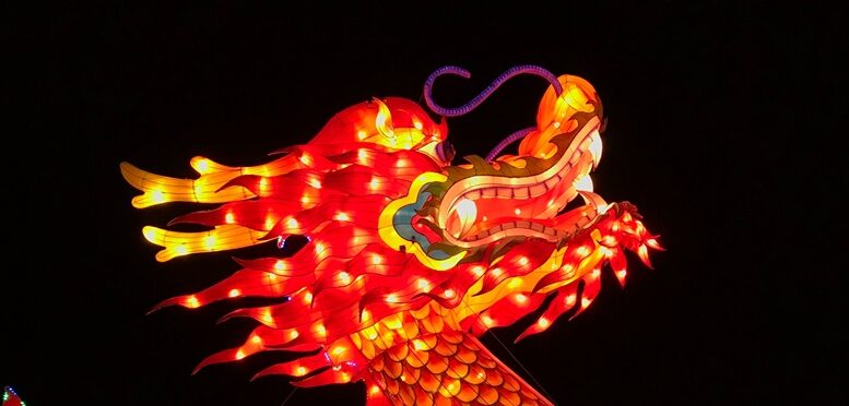 imagem de uma cabeça de dragão (boneco) grande, em vermelho e dourado, em contraste com um céu muito escuro.