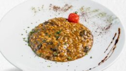 imagem de um prato fundo branco com risoto de fungui e decoração com um tomatinho cereja.