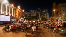 imagem de uma praça à noite, com uma tela de cinema , filas de cadeiras em frente e outras fileiras de bicicletas também de frente para a tela.