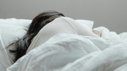 imagem de pessoa, aparentemente mulher, dormindo de lado, em uma cama com lençóis brancos.