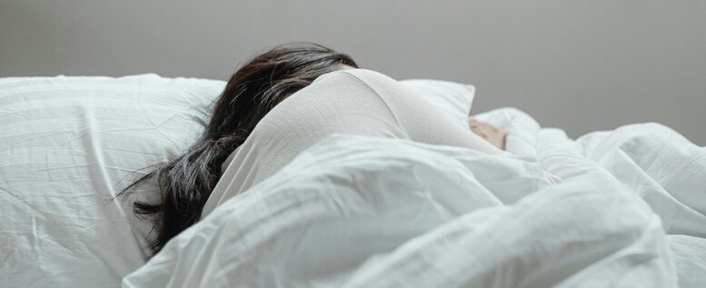 imagem de pessoa, aparentemente mulher, dormindo de lado, em uma cama com lençóis brancos.