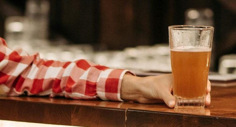 braço feminino apoiado em um balcão, segurando um copo de cerveja