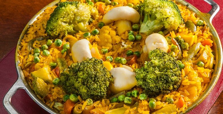 prato de paella vegetariana com cogumelos, brocoli e arroz de açafrão, em uma baixela de alumínio